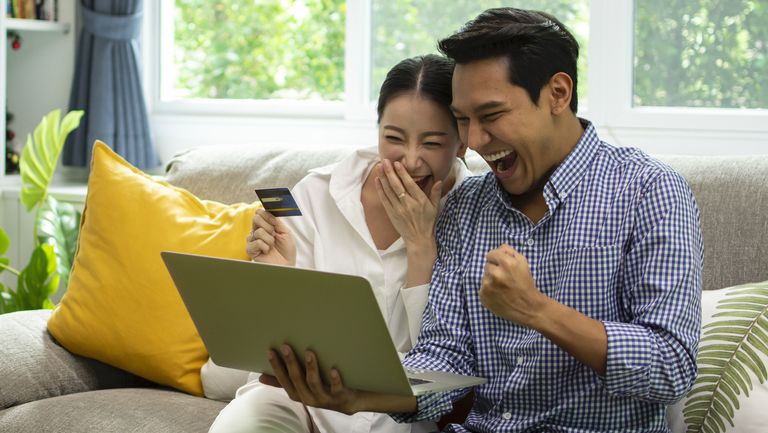 A couple rejoicing while looking at a laptop and holding a credit card