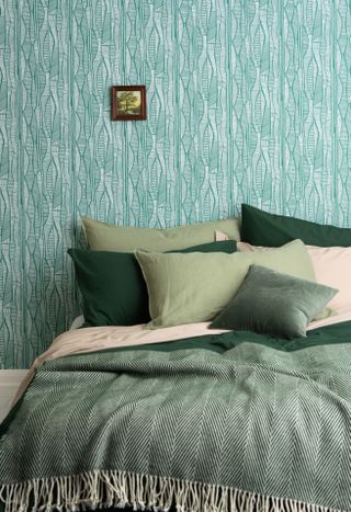 Blue print wallpaper with tiny landscape picture frame above bed with mixed green and light pink bedding