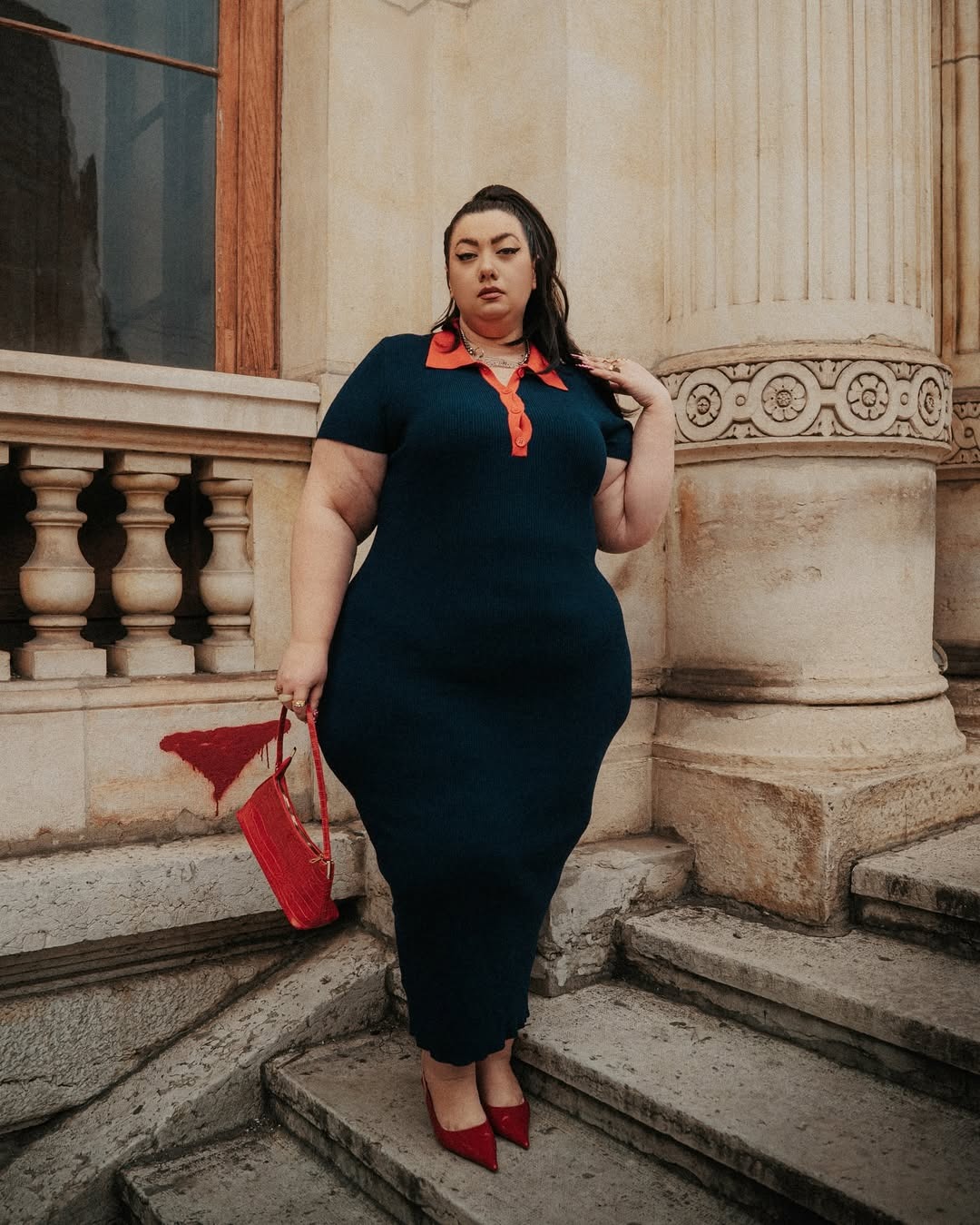Virginie Grossat wearing a sweater dress with red collar, red handbag, and red pumps.