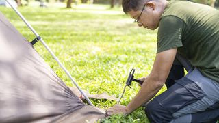 Man hammering a tent peg into the ground at campsite