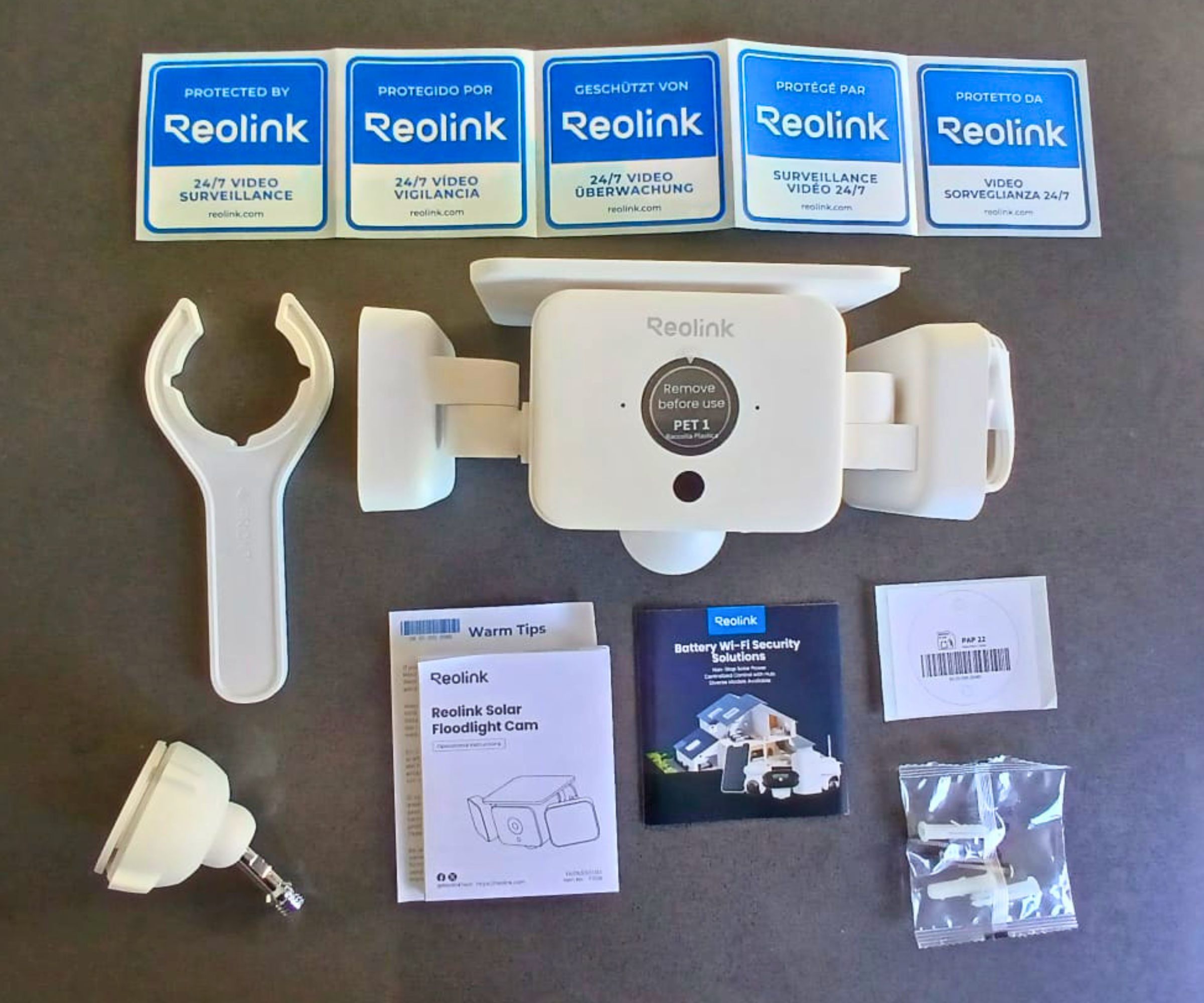 The contents of a Reolink Solar Floodlight Cam box laid flat, including the camera unit, mounting hardware, spanner tool, instruction manual, multilingual security stickers and fixings.