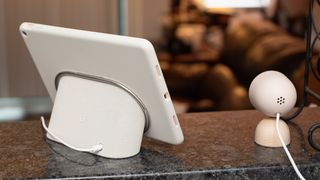 Google Pixel Tablet står på en köksbänk på sin laddningsstation bredvid en övervakningskamera.