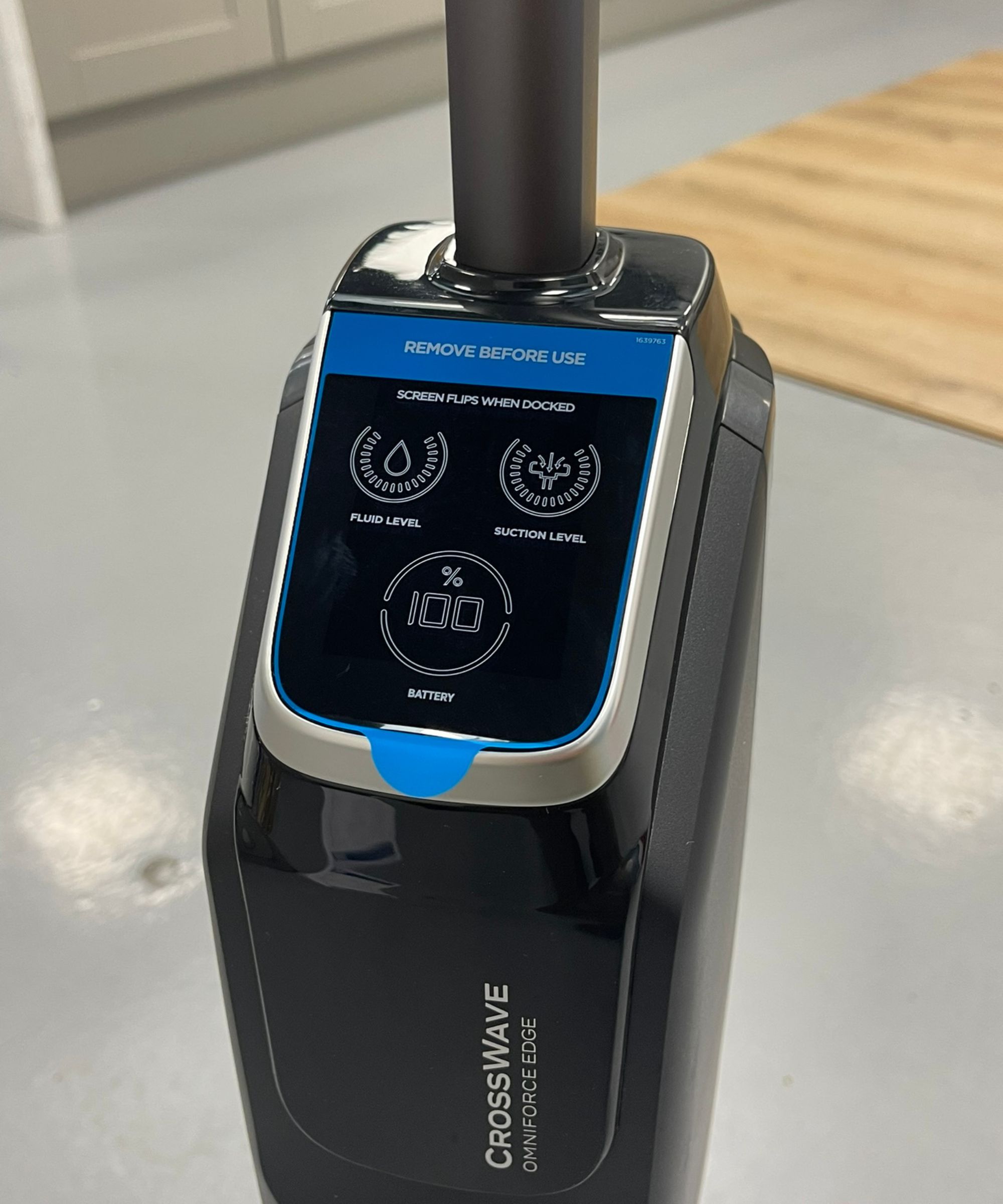 Closeup of the Bissell CrossWave OmniForce Edge screen showing battery life, fluid level and suction level, on gray linoleum floor in Future test center with wooden floor panels and gray cabinets pictured in background.