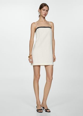 Model wears a white mini dress with spaghetti straps and black trim on the top by Mango