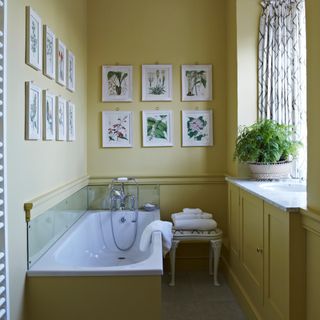 coastal bathroom with yellow walls, botanical artwork on walls, marble basin, small stool, white towels, plant