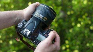 A Nikon D800 with the Nikon AF-S 85mm f/1.4G prime lens in front of a green, bokeh-filled background