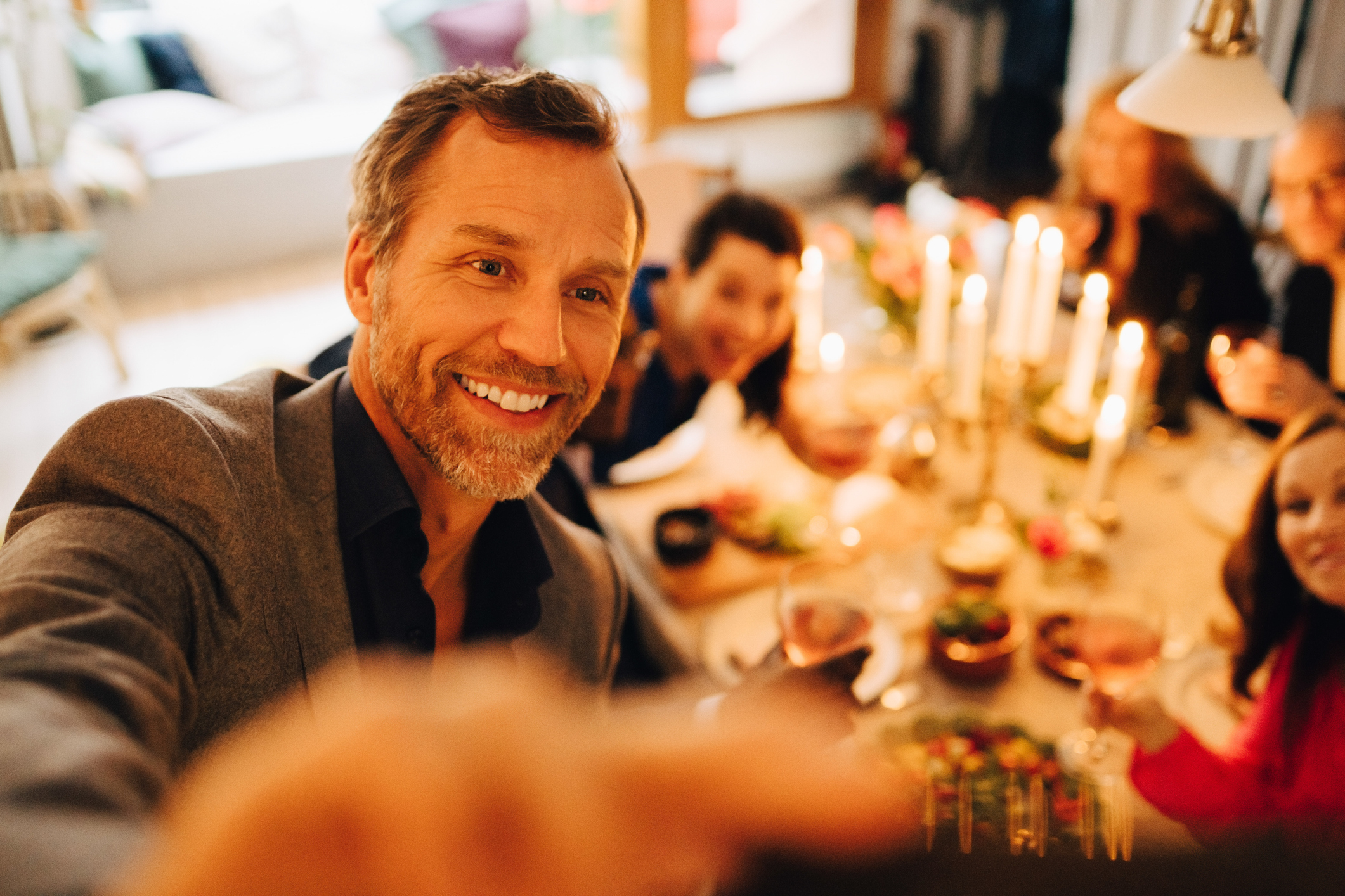 An older man takes a selfie of himself and friends at a dinner party.