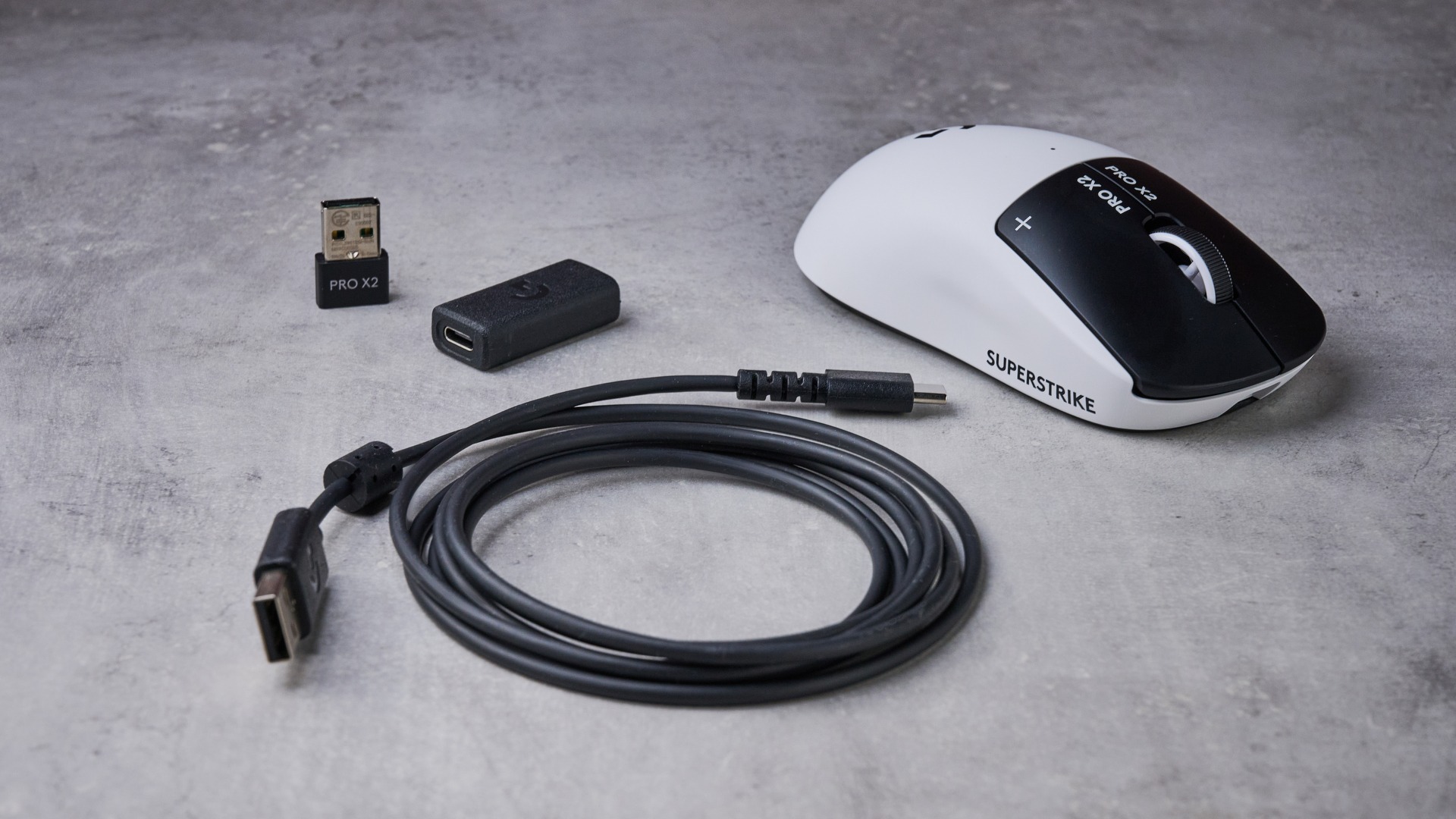 USB cable, USB dongle, and extender for Logitech G Pro X2 Superstrike, as well as Logitech G Pro X2 Superstrike itself, on white desk