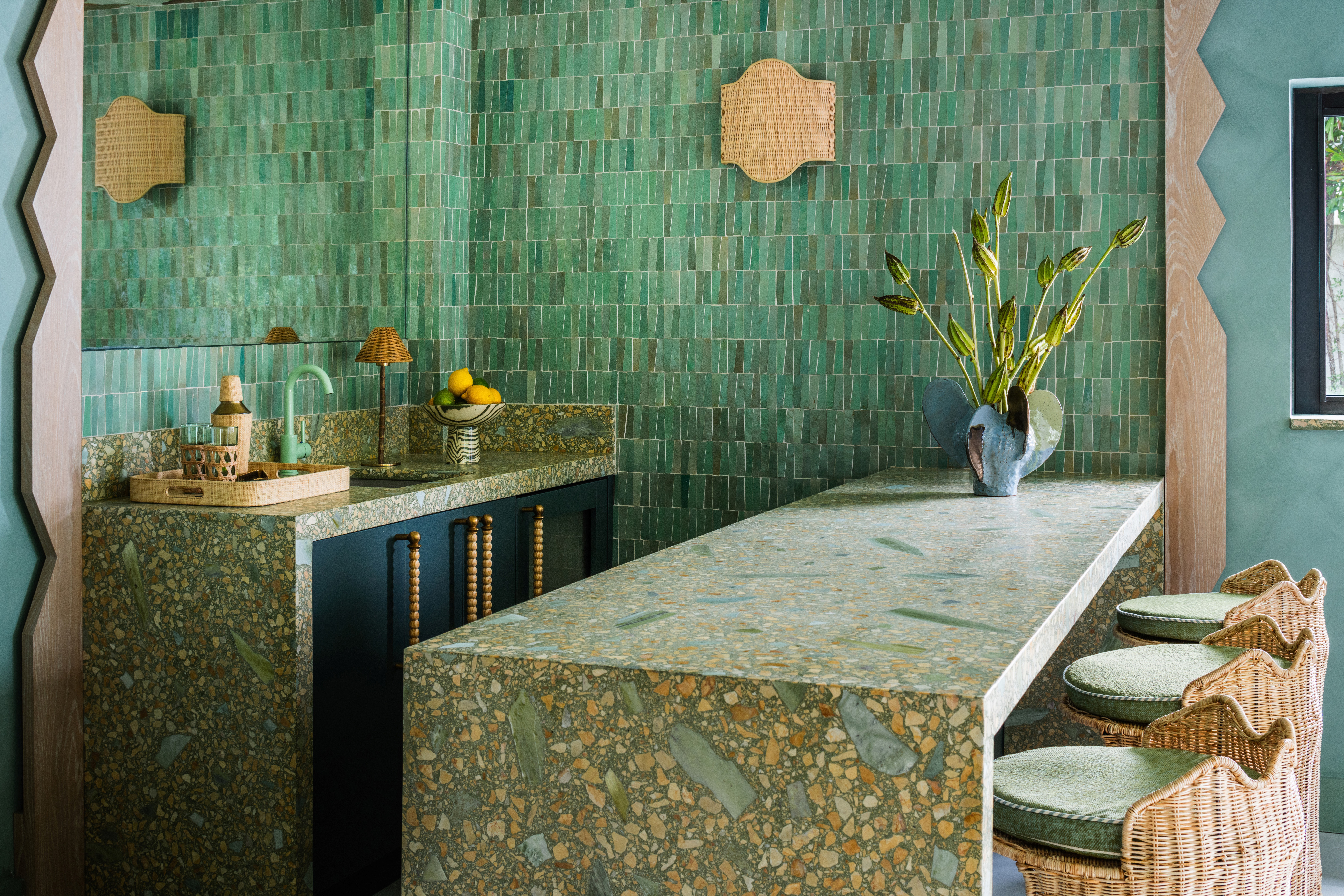 Interior of a tropical home with teal walls, zellige tiles surfaces, wavy, sand-coated details, rattan furniture mixed with bright aquamarine and ochre touches, and a botanical-themed mural ceiling.