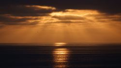 Sun breaking through clouds over the ocean and coloring the sky orange