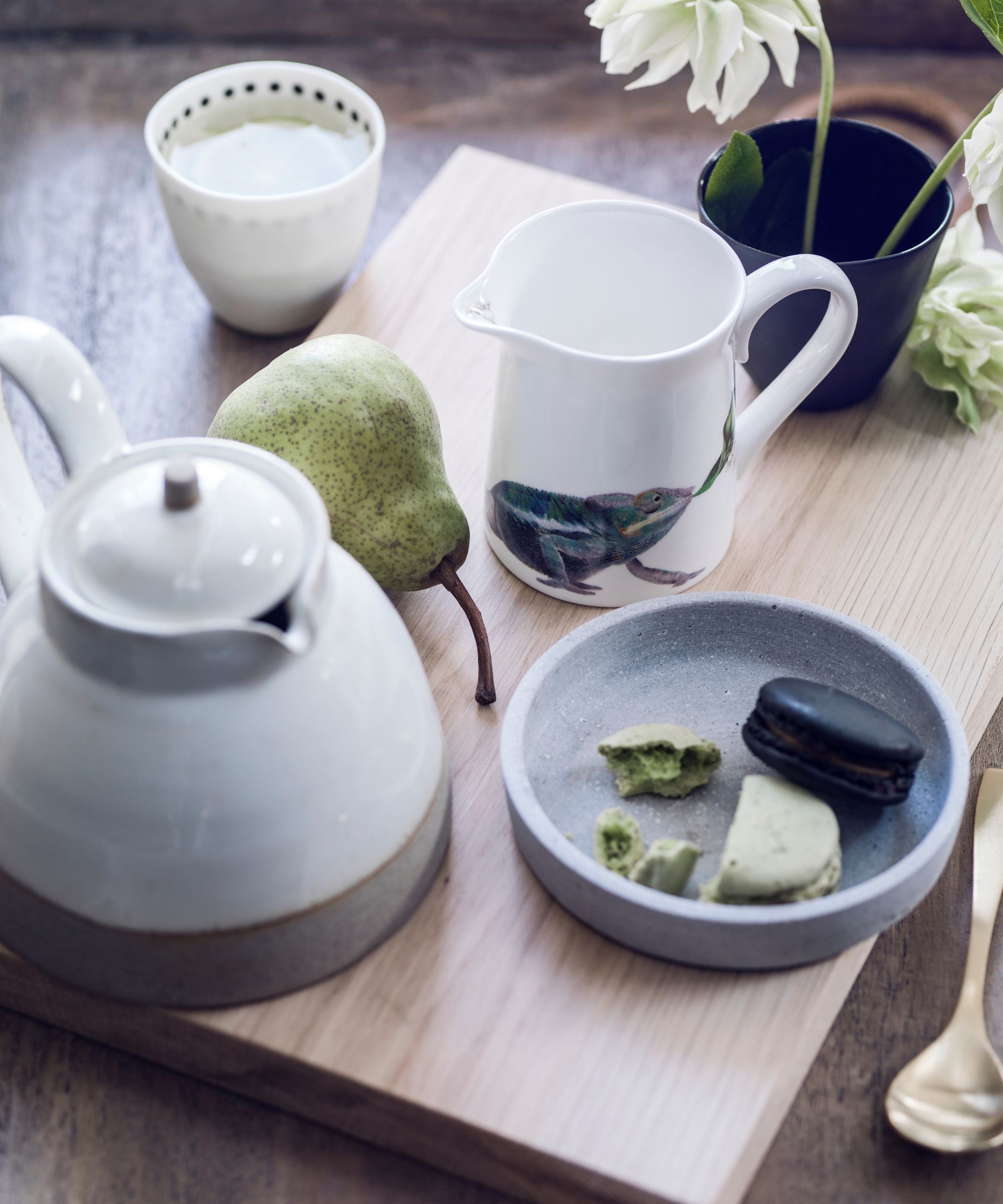 Tea pot and jug on wooden board with bowl of macarons