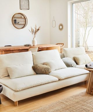 A white living room with a white couch, wooden dining table, and jute rug