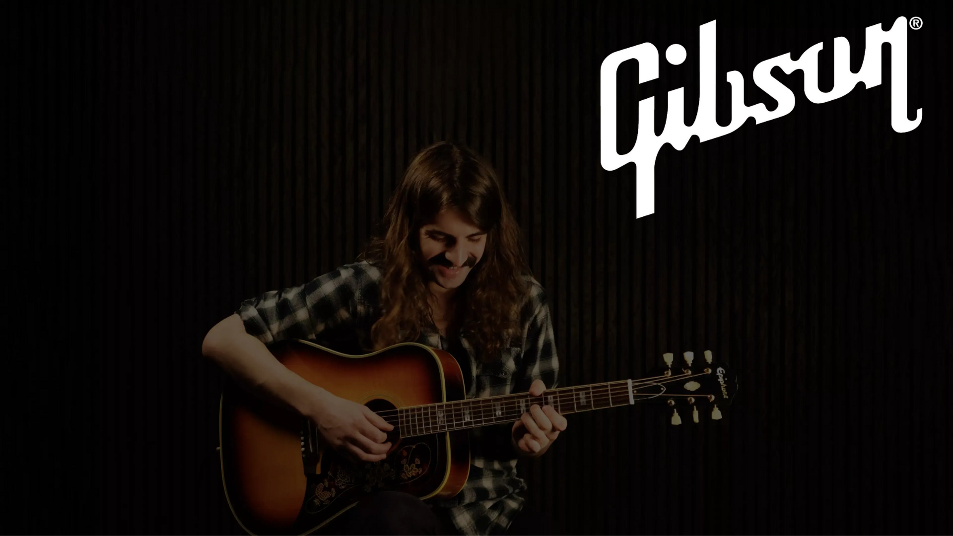 A smiling man plays an acoustic guitar