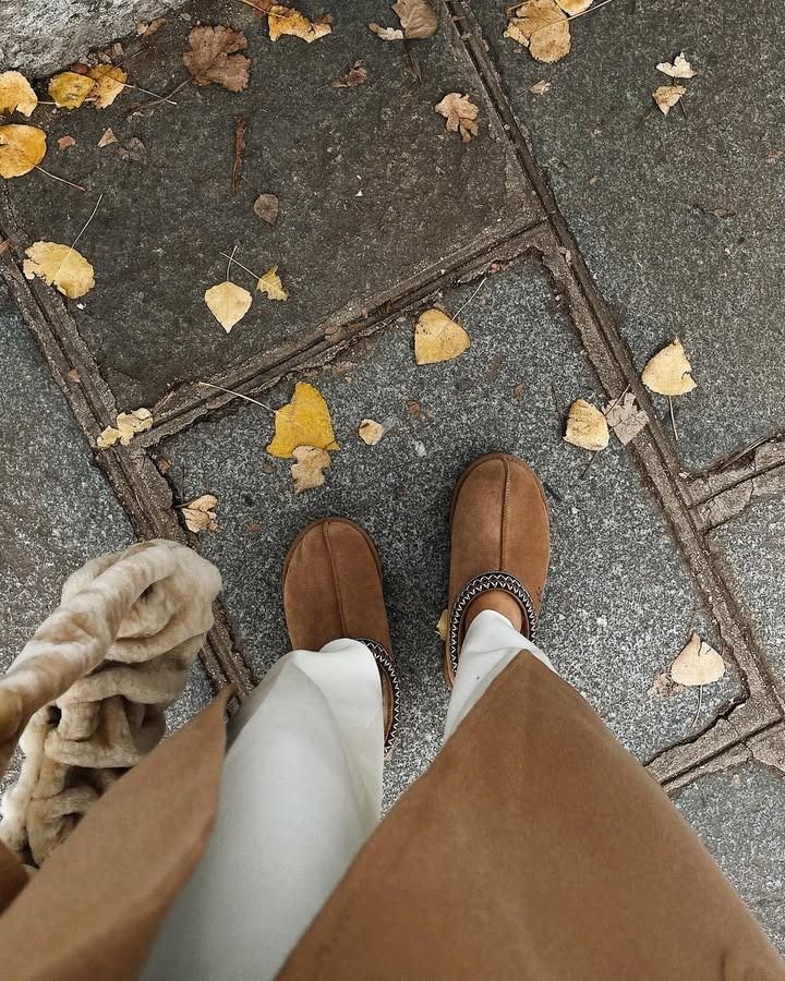 Influencer Julia Mateian wears Ugg clogs with white pants and a brown coat.