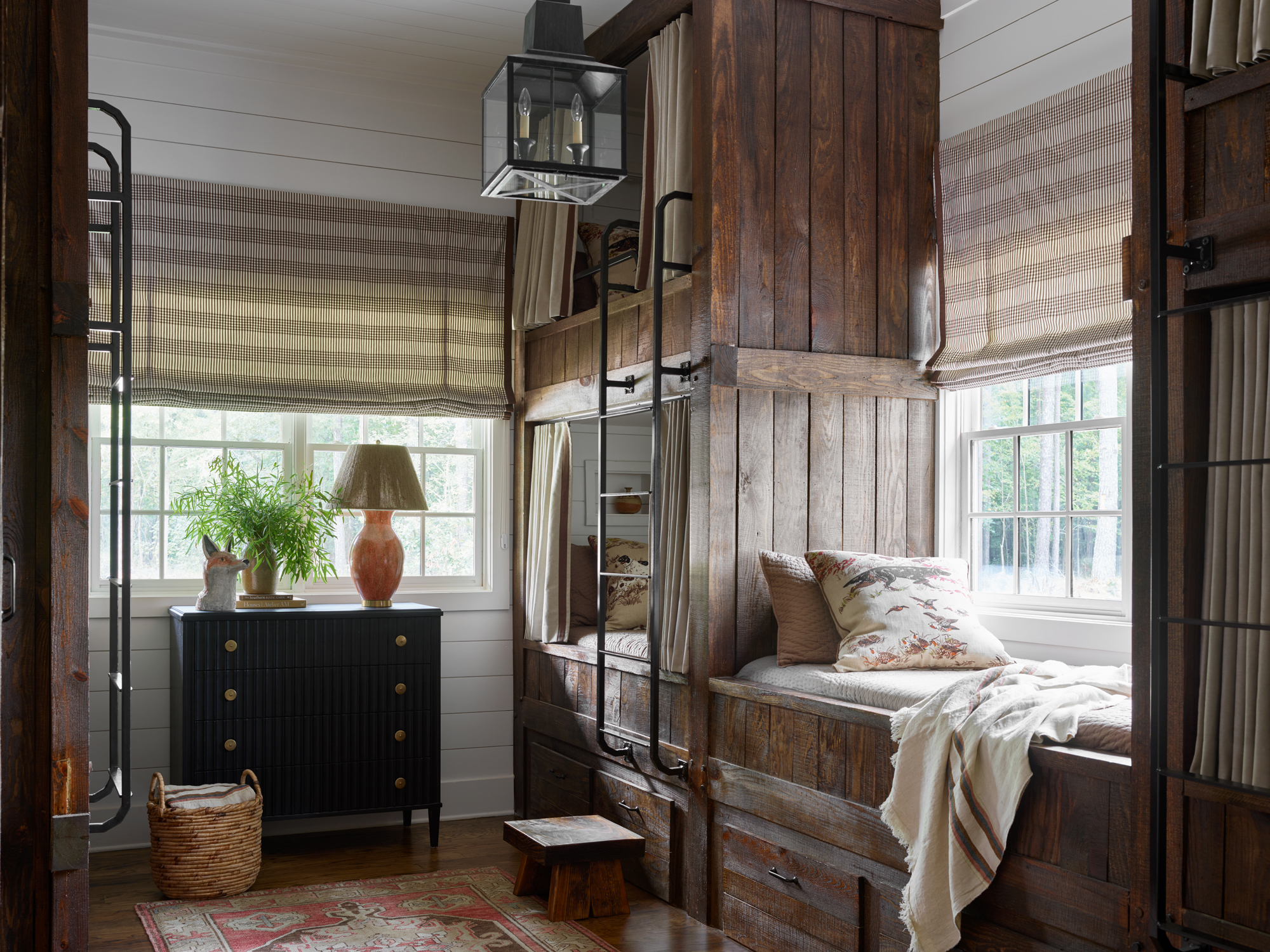 Bedroom with built-in wood panelled bunk beds, ship lap walls, persian rug, chest of drawers with vase and lamp and stripey blinds