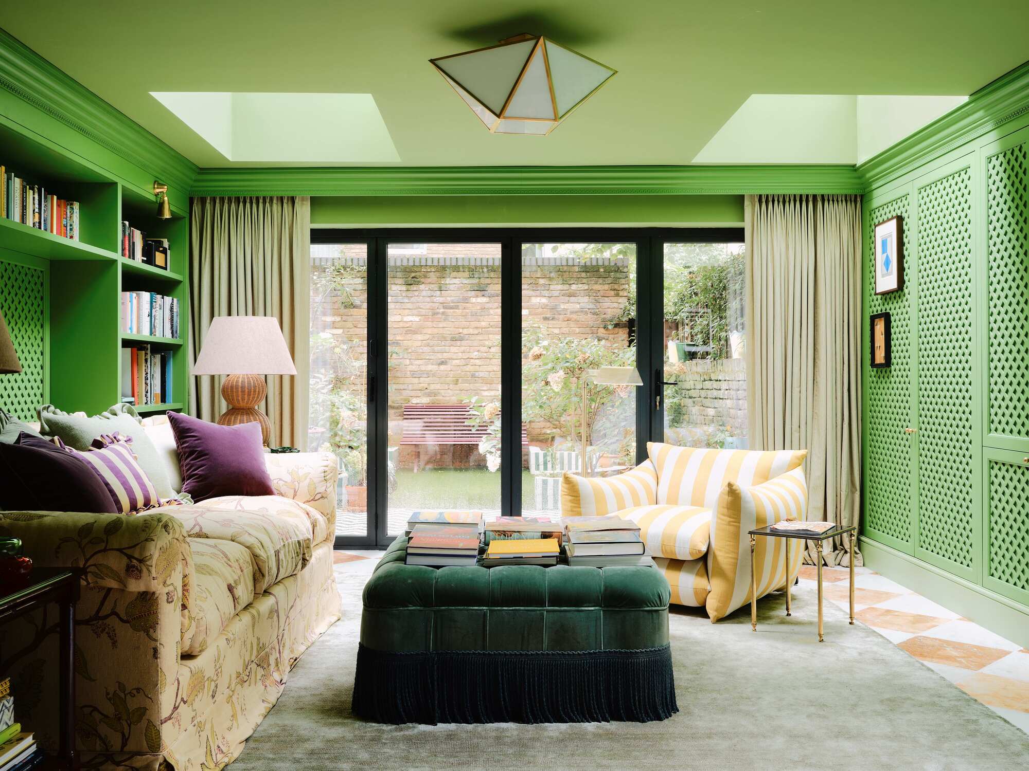 bright green modern living room with roof windows, plush green ottoman, floral sofa, with checkered floors, yellow striped armchair, and green carpet