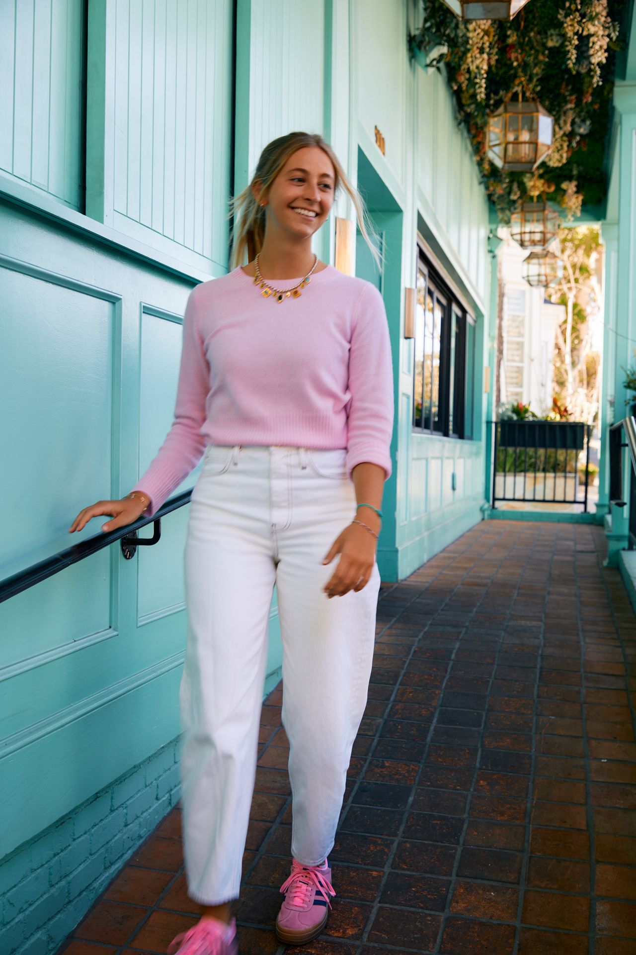 girl wearing pink sweater, white jeans and neon pink adidas.