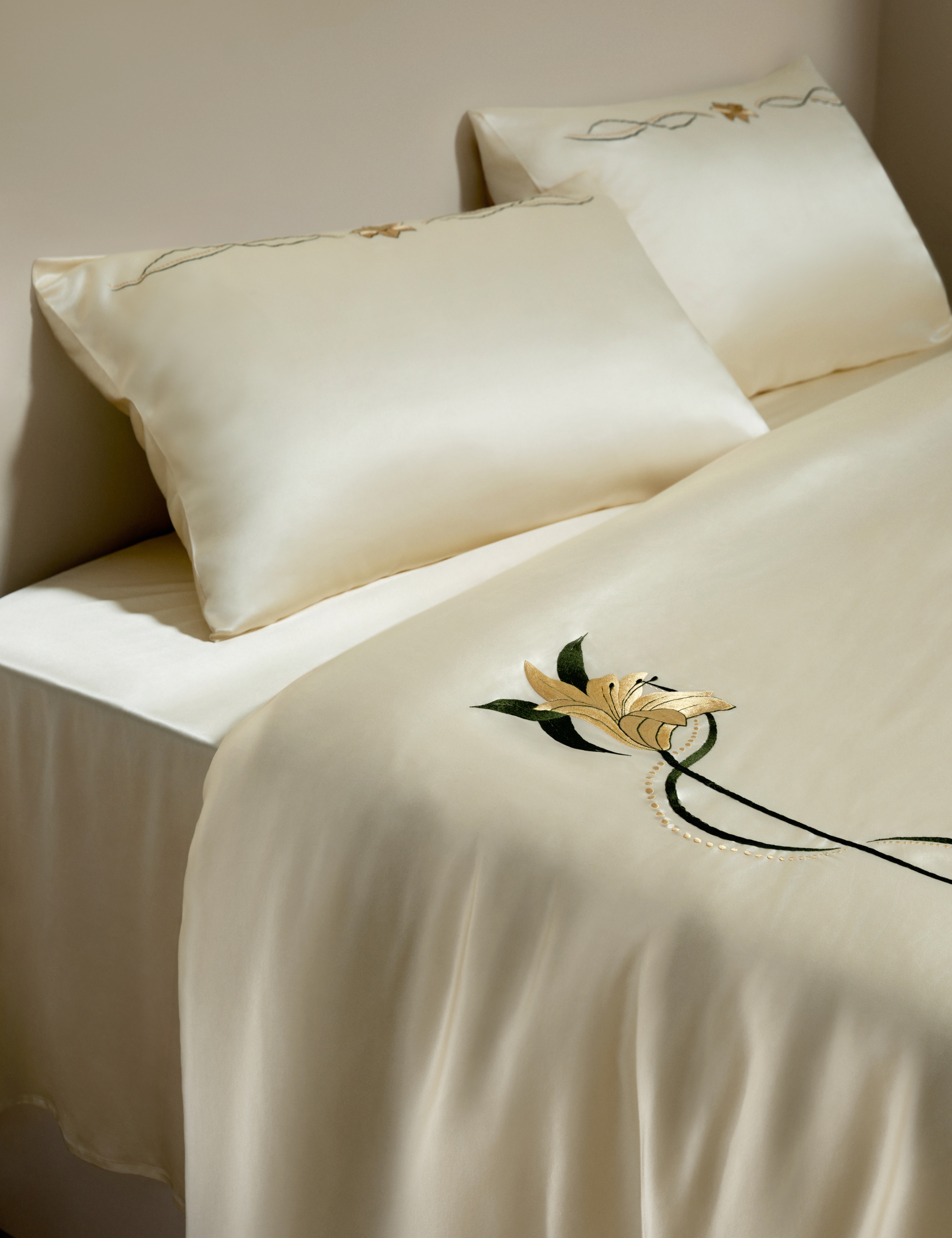 Lily-embroidered cream silk bed linens photographed in a neutral bedroom