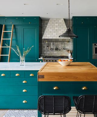kitchen countertop trends, teal kitchen with wooden butcher block at one end of island, marble the other, tiled backsplash and cooker hood, ladder, teal painted cabinetry