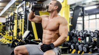 Man sitting on a workout bench drinking from protein shaker during resistance workout
