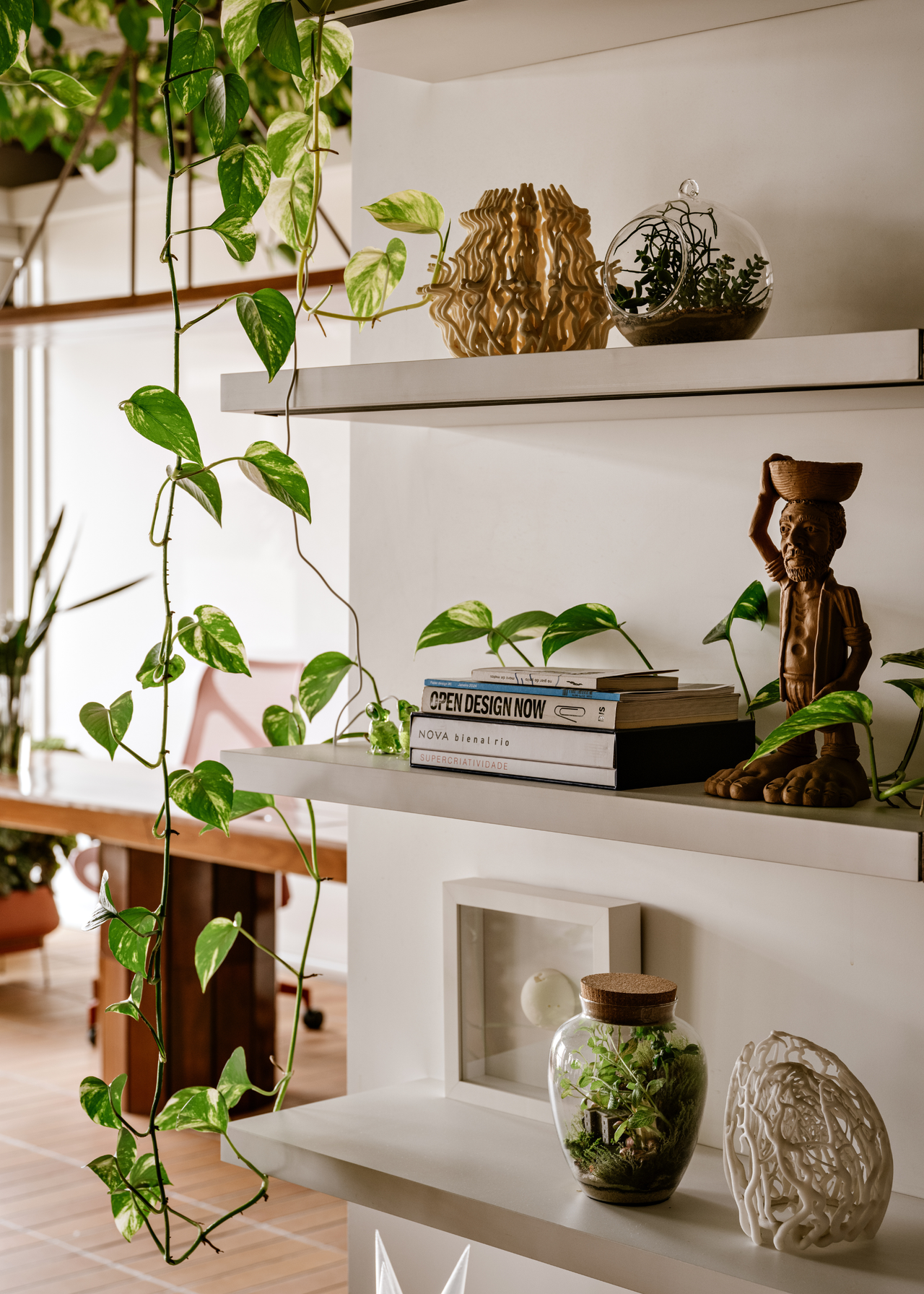 A close-up of a white book shelf with books, decor and mini terrariums
