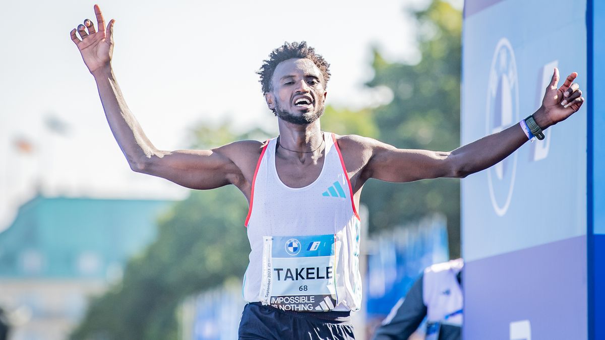 Tadese Takele crosses the line with his arms in the air at the Berlin Marathon, wearing a white vest and black shorts.