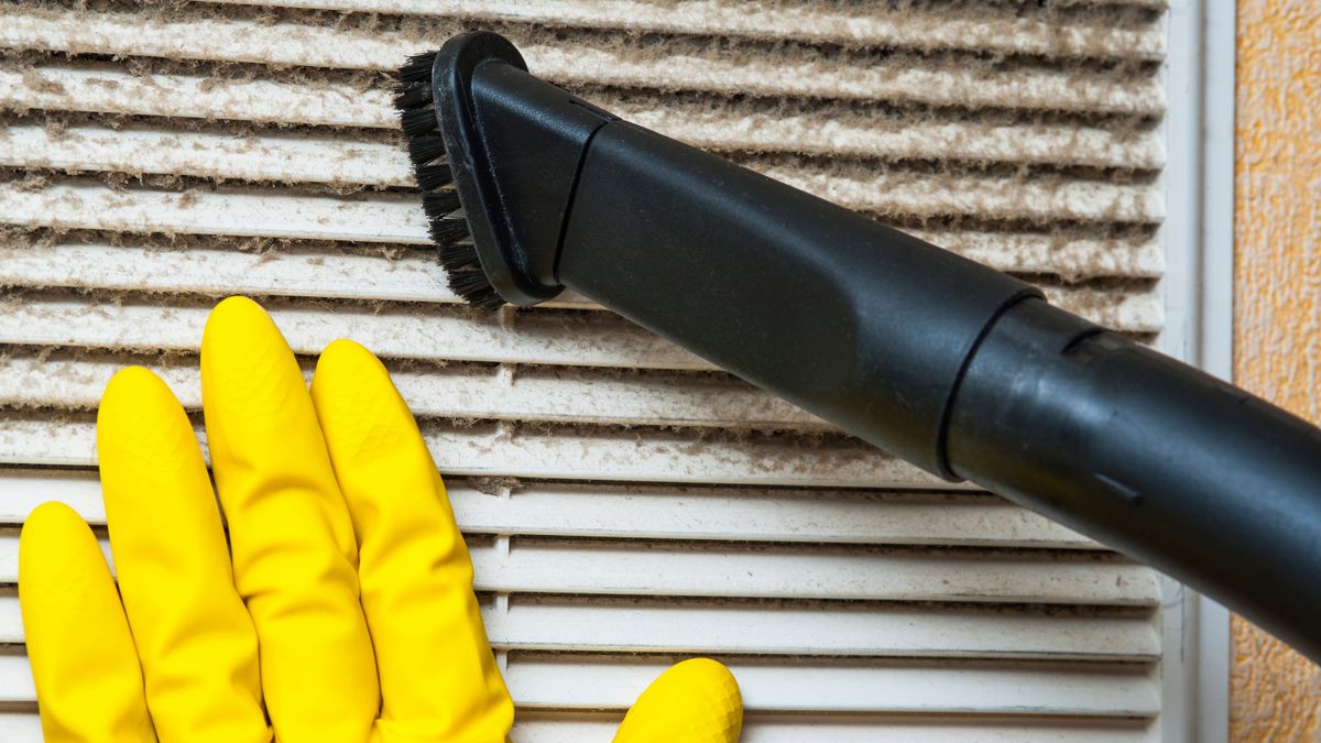 hand wearing yellow rubber glove holding dusty filter with vacuum nozzle in shot removing dirt