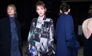 Four female models wearing looks from Costume National's collection. One model is wearing a blue piece with ruffles and a dark blue coat. Another model is wearing a black and white piece with a floral block print design and dashes of colour. The third model is wearing a dark blue piece. And the fourth model is wearing a dark blue piece which exposes part of the back