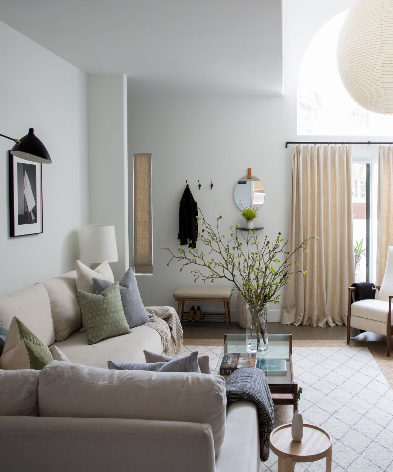Small entryway area hidden behind curtain beyond space with sofa, cream diamond pattern rug