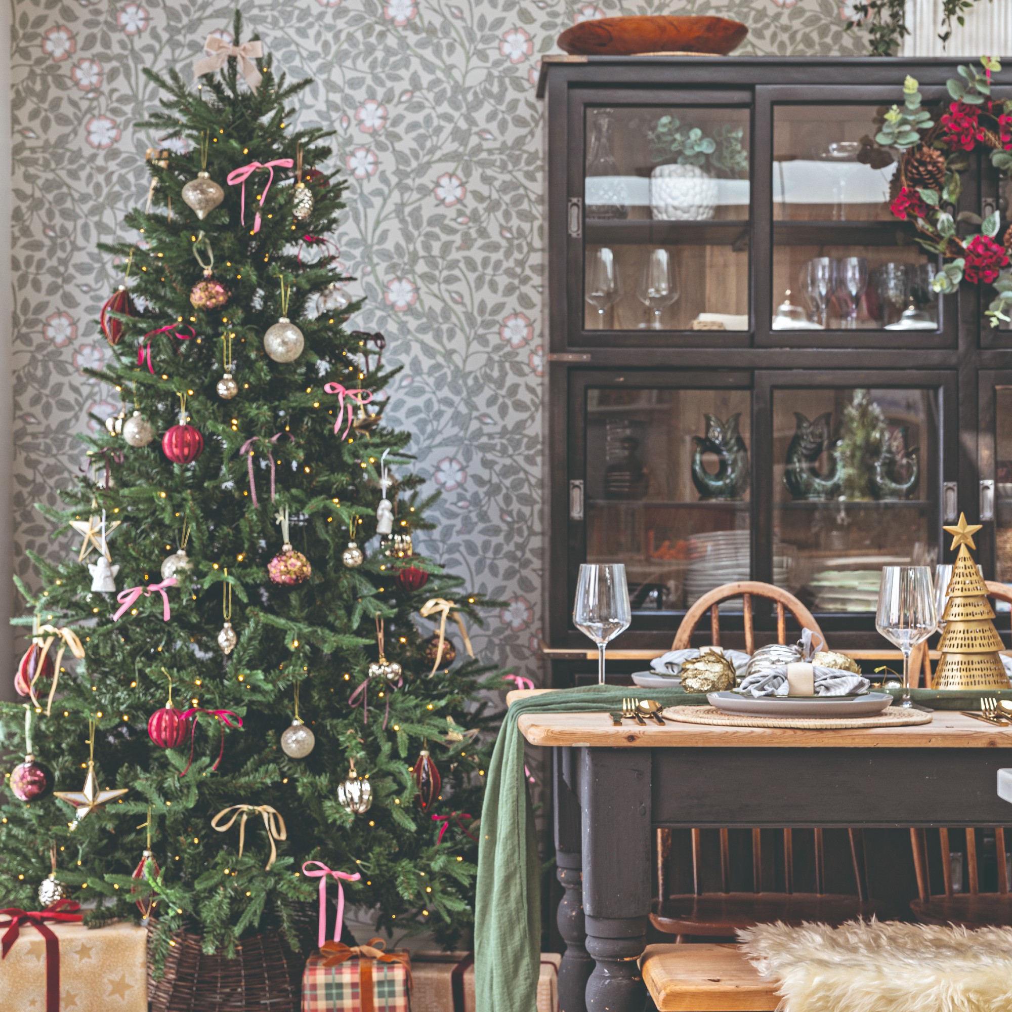 A dining room covered in a botanical-print wallpaper decorated for Christmas with a traditional Christmas tree