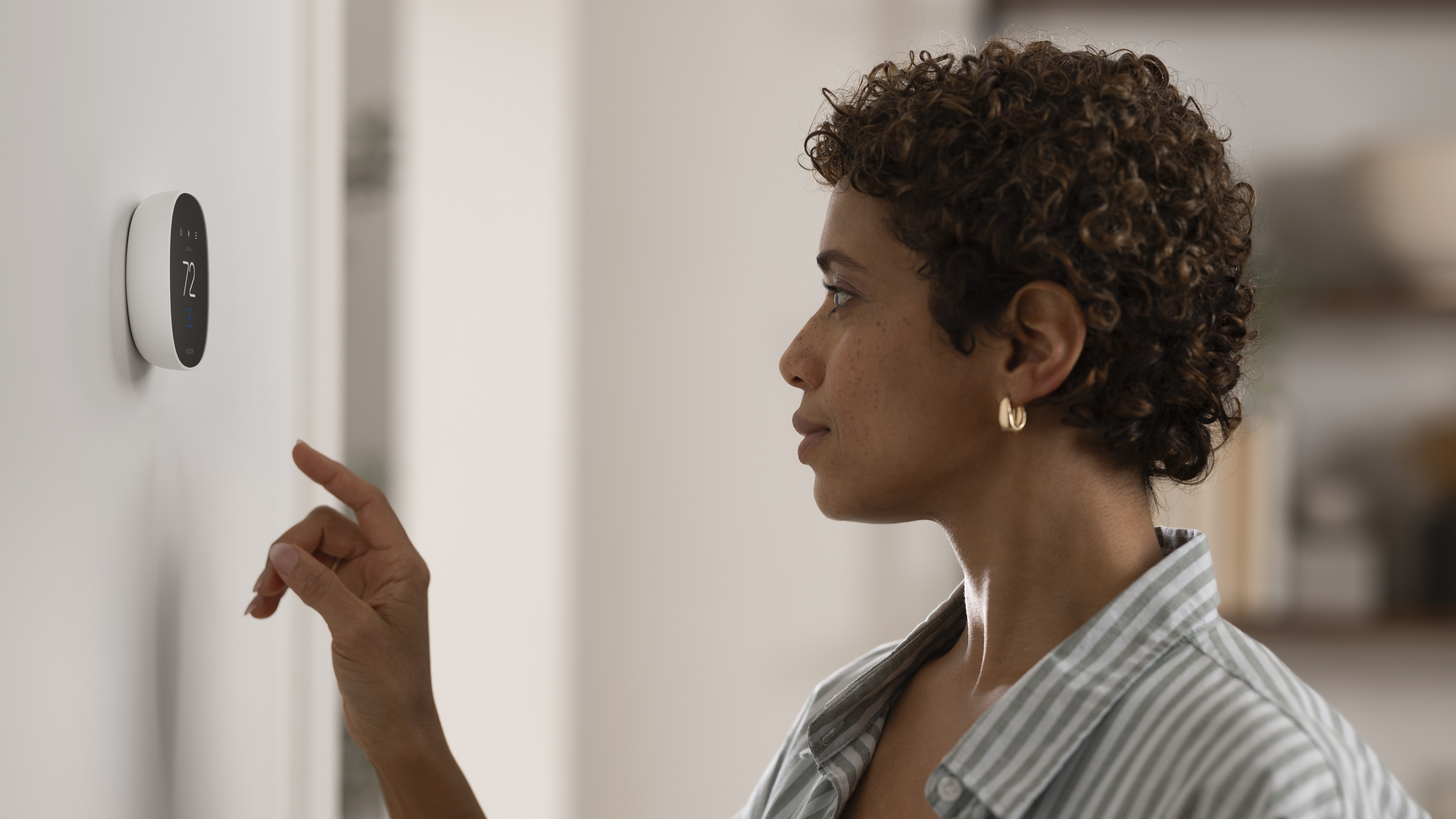 Woman using Ecobee Smart Thermostat Essential installed on wall