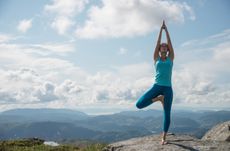 Young woman practicing yoga high up on top of mountain Ulriken, in Bergen, Norway, overlooking mountain range - tree pose or Virksasana.