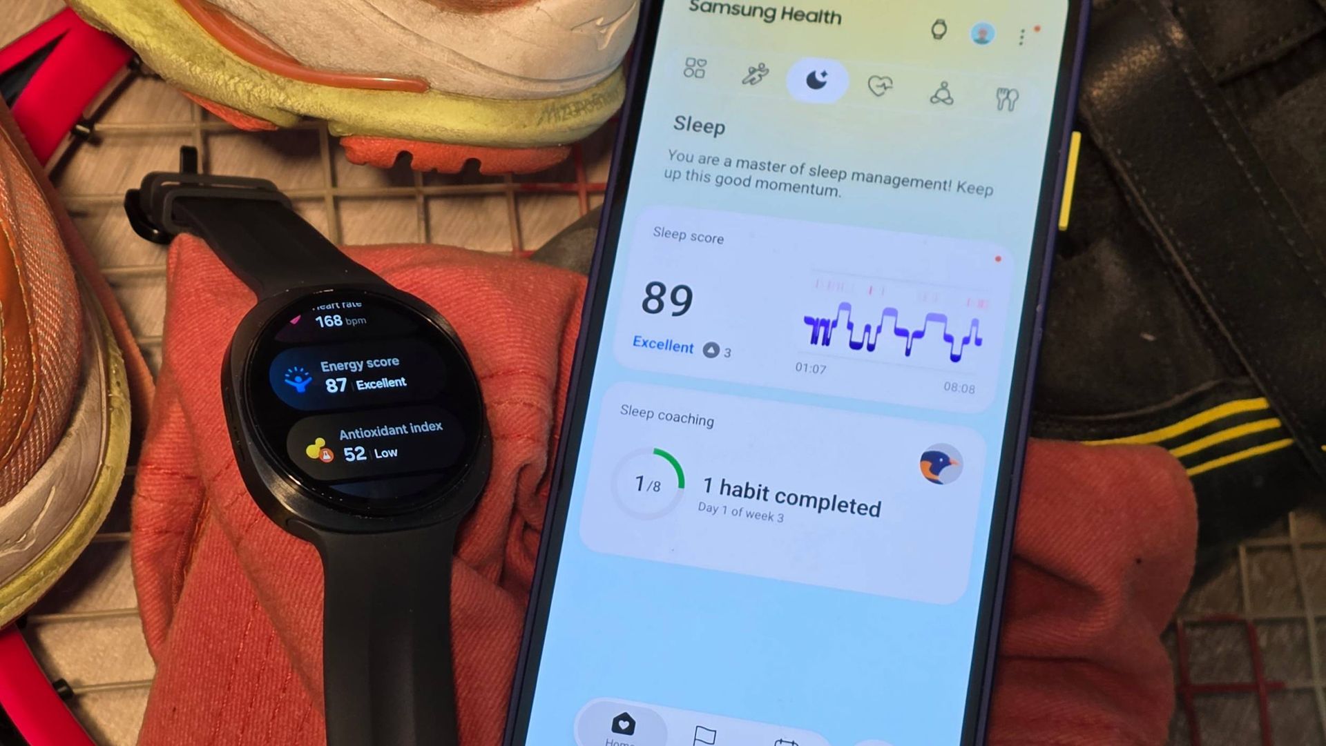 The Samsung Galaxy Watch 9 on some sports kit, next to a smartphone showing Samsung Health.