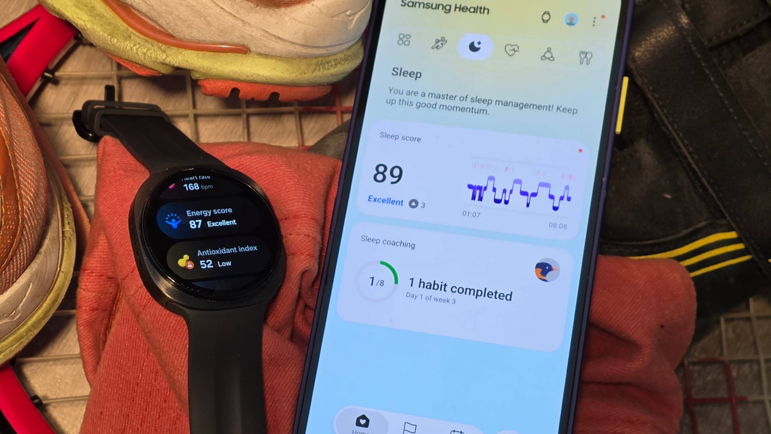The Samsung Galaxy Watch 9 on some sports kit, next to a smartphone showing Samsung Health.