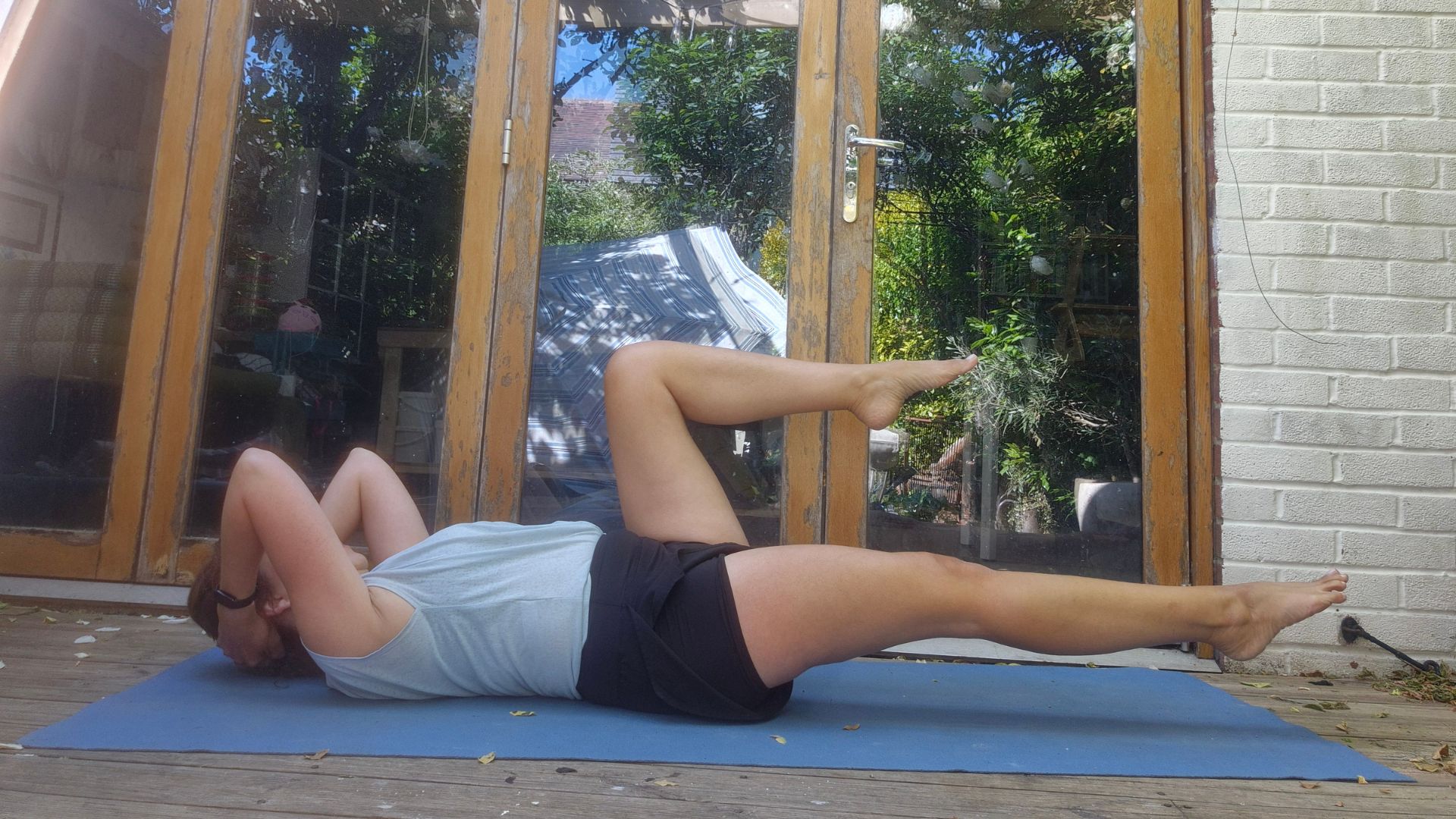 Kerry Law doing the Meredith Shirk workout lying down on yoga mat in back garden, doing core exercise