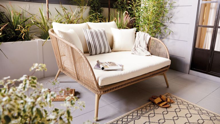 outdoor snug seat in natural tones with cream cushions on an outdoor rug