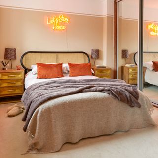 Bedroom with rattan headboard, neutral coloured throws and neon sign over the bed
