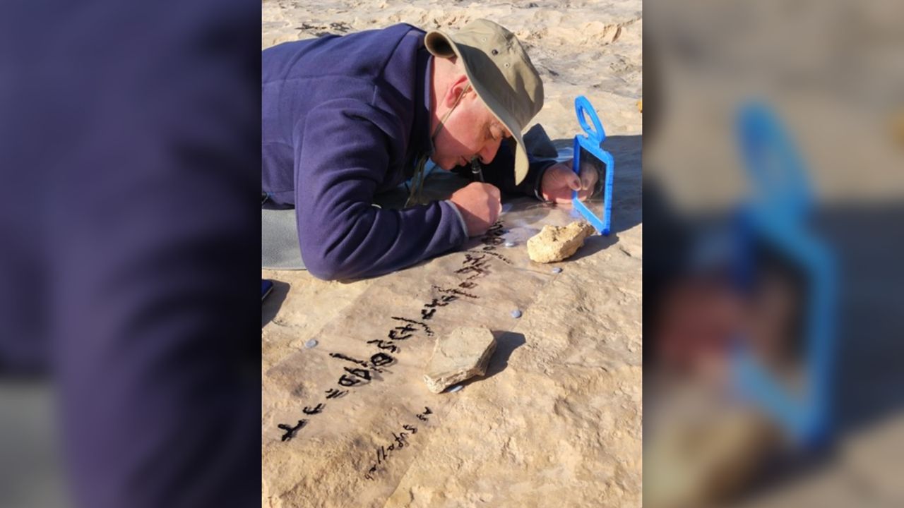 A man lays on his stomach on the ground as he outlines and examines petroglyphs.