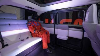 A futuristic interior of a vehicle is shown with black floors and white seats. In the spacious back sits Campos, a manikin in an orange Artemis flight suit. Campos flew aboard the Orion spacecraft during the Artemis I mission in order to collect important data that will prepare astronauts for future Artemis missions.