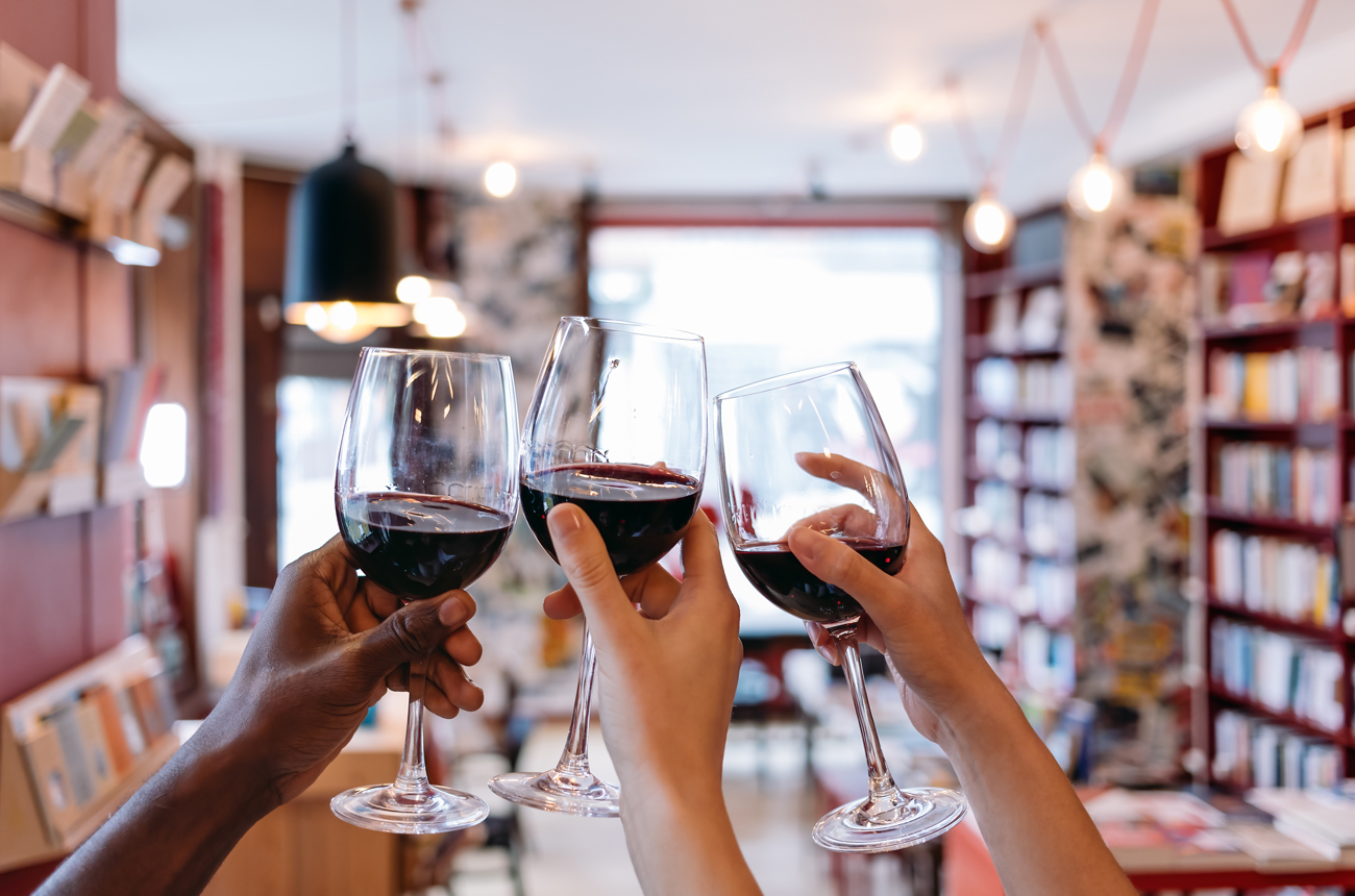 Three hands holding glasses of red wine in book shop