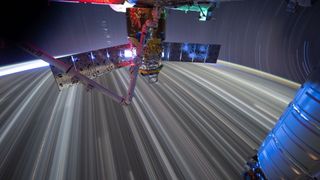 colorful streaks of light far below a T-shaped spacecraft in the foreground