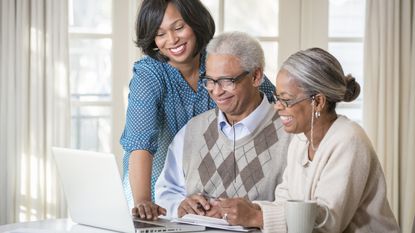 A woman and her elderly parents smile as they look at a laptop together.