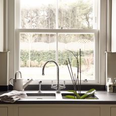 Kitchen sink underneath a large window looking out onto a garden. An orchid is sitting in the sink