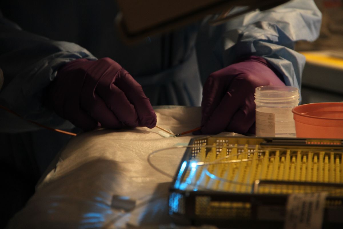 A doctor holds a laser, shining a blue light, during a medical procedure.