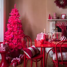 A dining room with a bright pink Christmas tree in the corner and tonal red dining table, chairs and decor