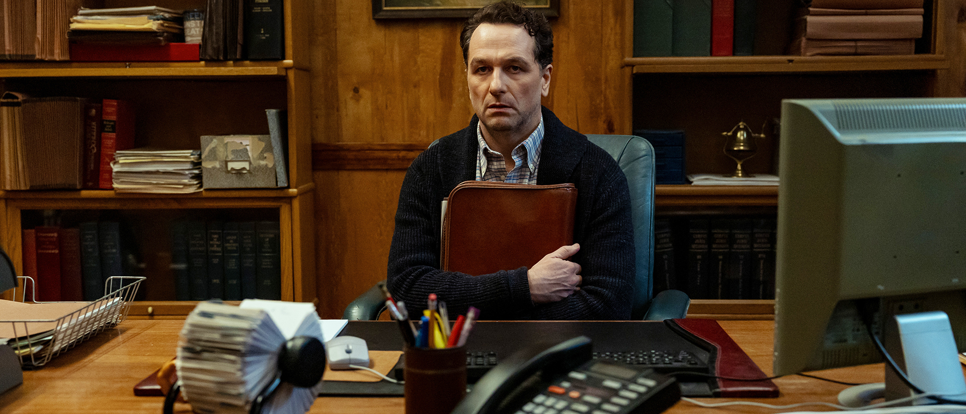 Tom Loftis sitting at his mayoral desk and clutching a leather documents holder in Widow's Bay