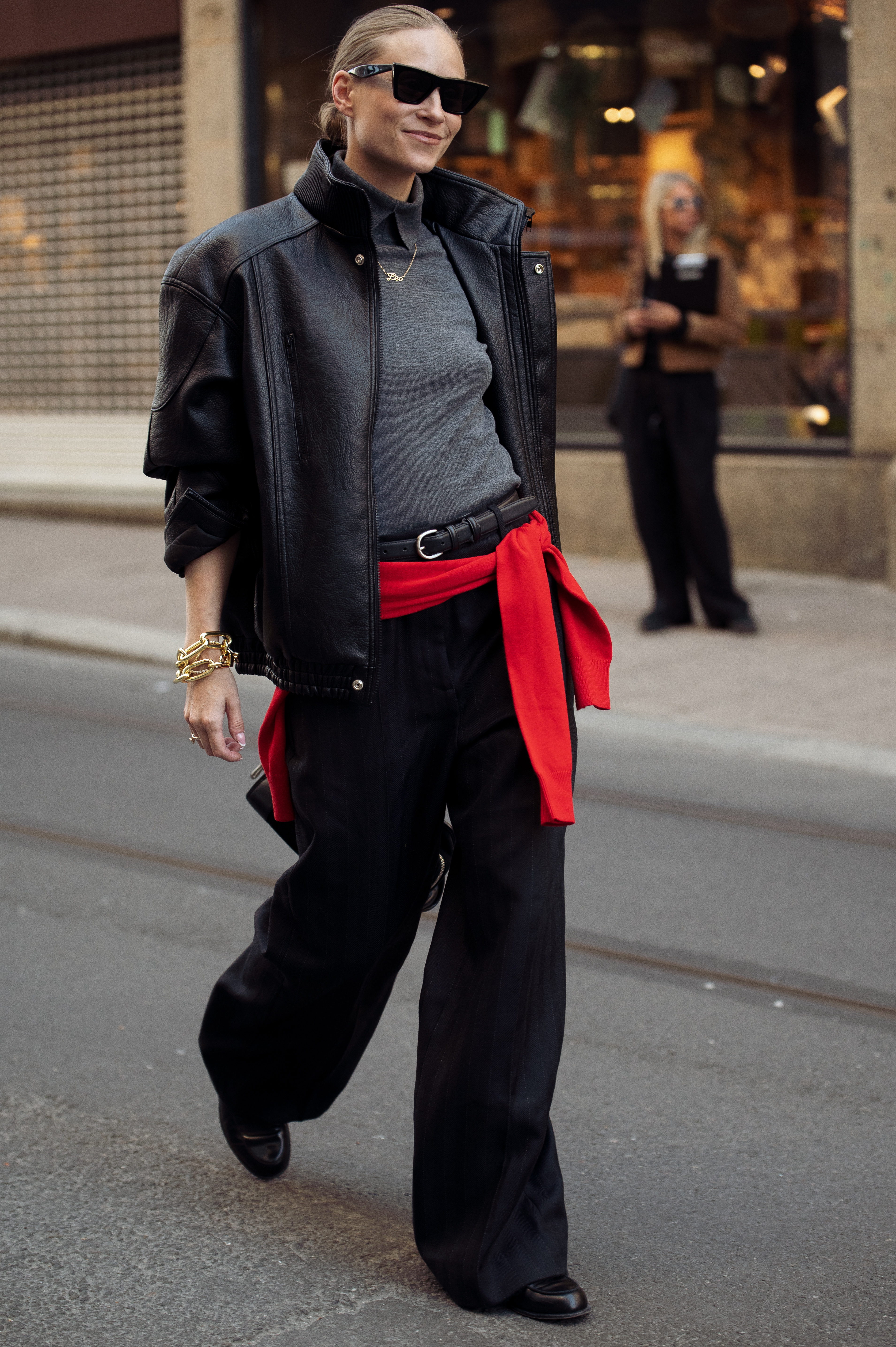 Tine Andrea wears black trousers, grey top, black leather funnel neck jacket and red scarf over her hips in Oslo