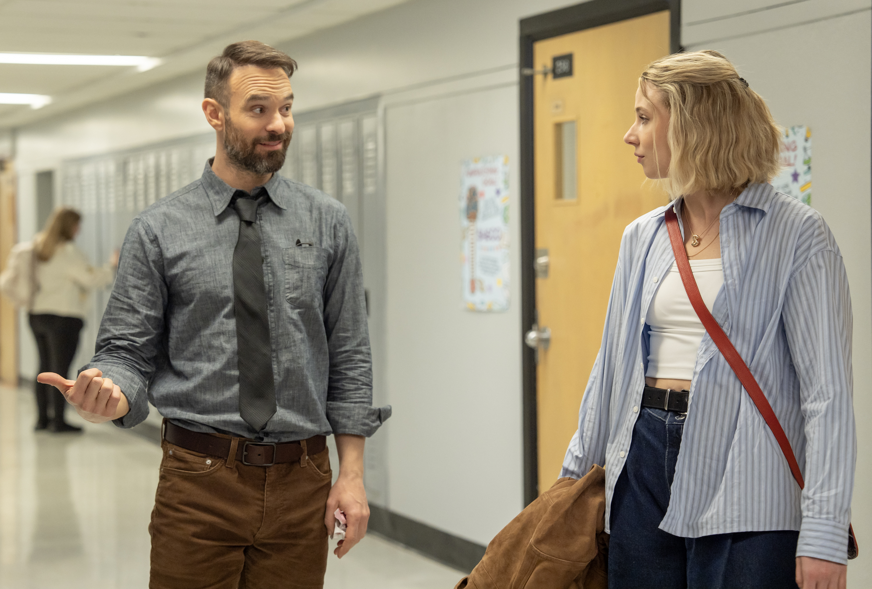 Two adults (Charlie Cox as Mr. Teacher, Lucy Freyer as Billie) stand in a high school hallway, in 'Adults.'