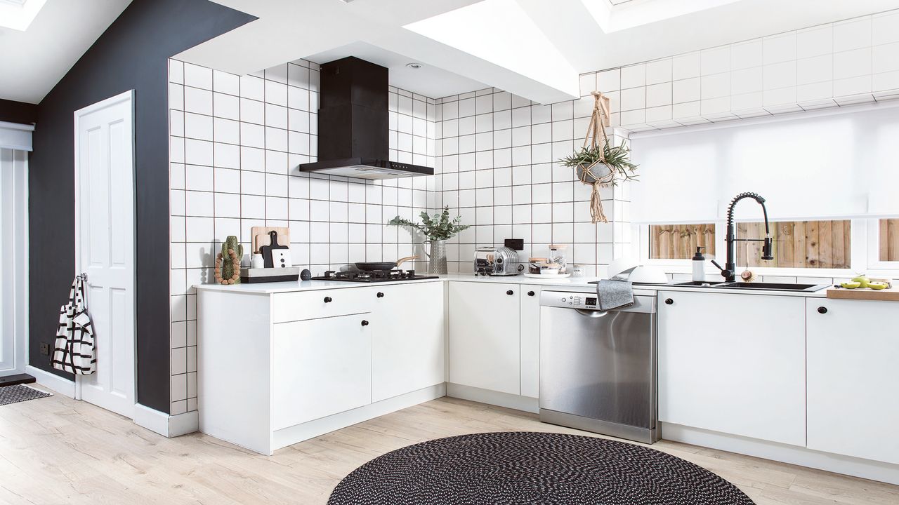 monochrome kitchen with white cabinets and tiles, a black wall and rug and wooden flooring 