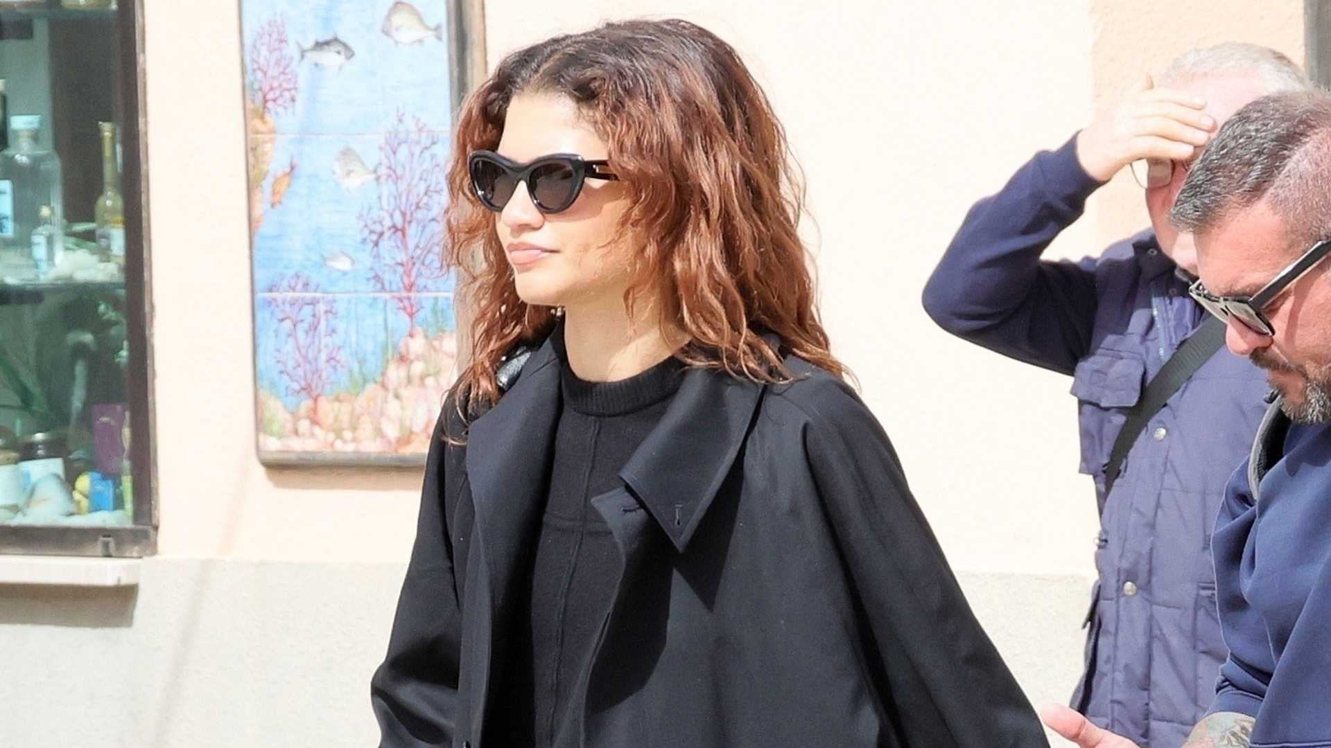 Zendaya walks in Italy wearing a black trench coat and straight leg jeans